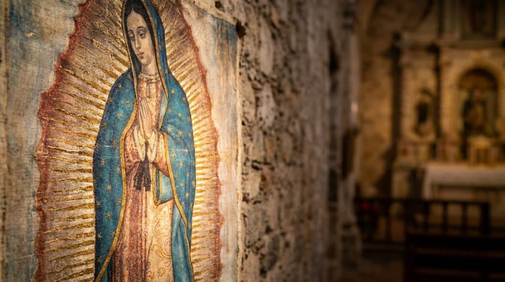 Représentation de Notre-Dame de Guadalupe sur un mur de pierre dans une église floue.
